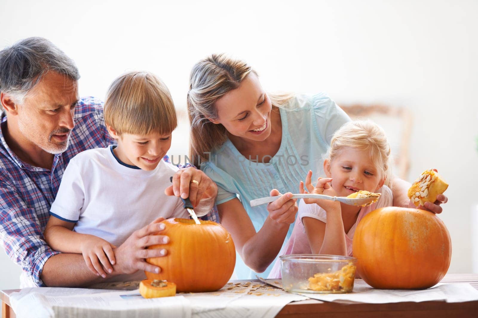 Family, halloween and carving a pumpkin with children in a home for fun and bonding. Man and woman or parents and young kids together for creativity, holiday lantern and happy craft at a table.