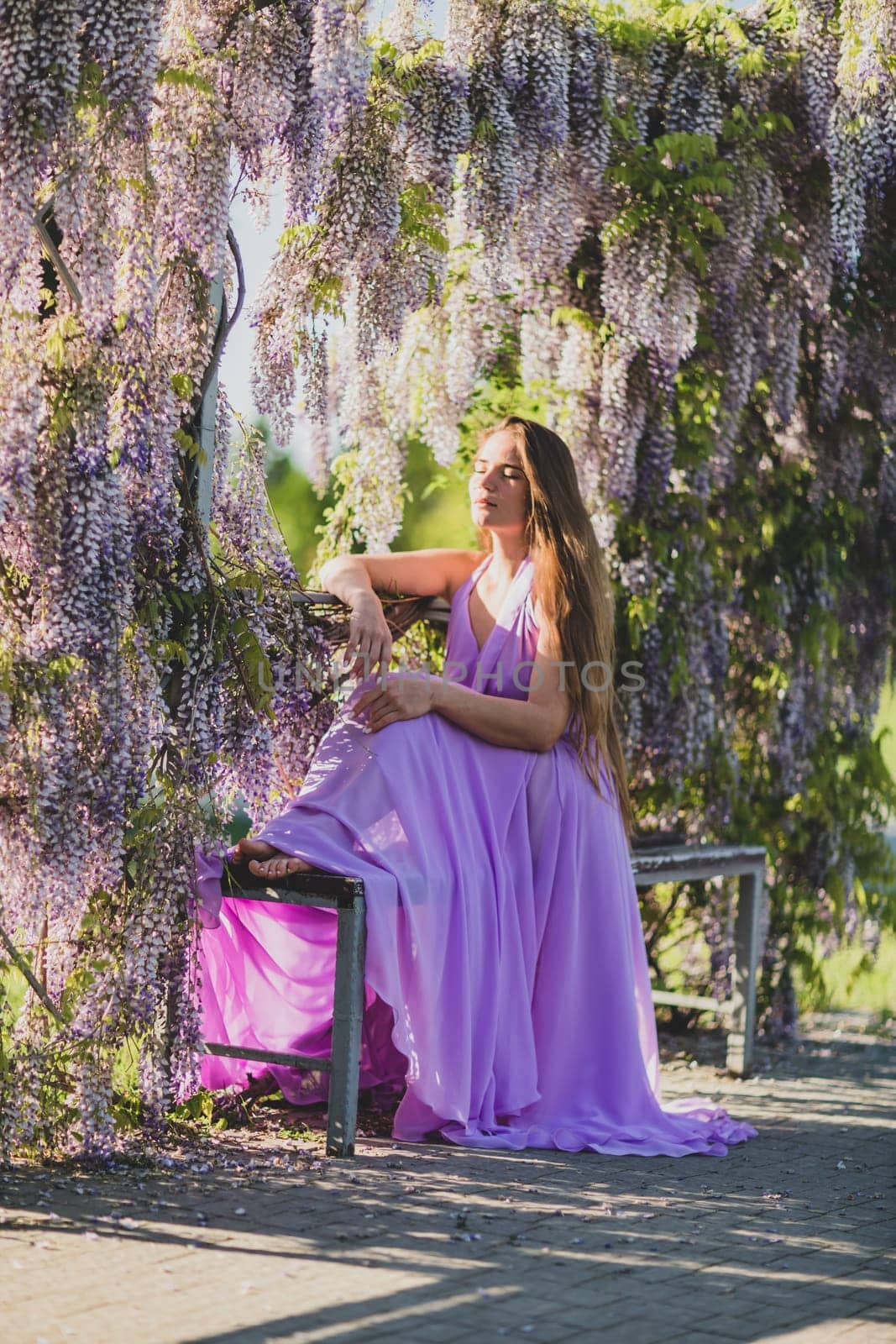 Woman wisteria lilac dress. Thoughtful happy mature woman in purple dress surrounded by chinese wisteria by Matiunina