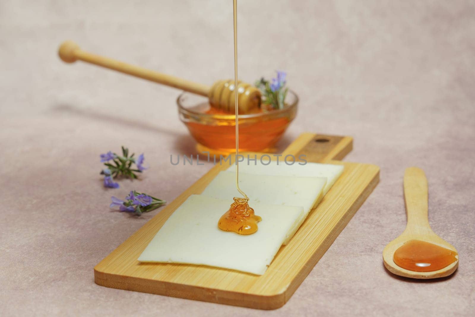 drizzle of honey dripping on cheese slices with fresh rosemary branches in bloom and a glass bowl with rosemary honey.