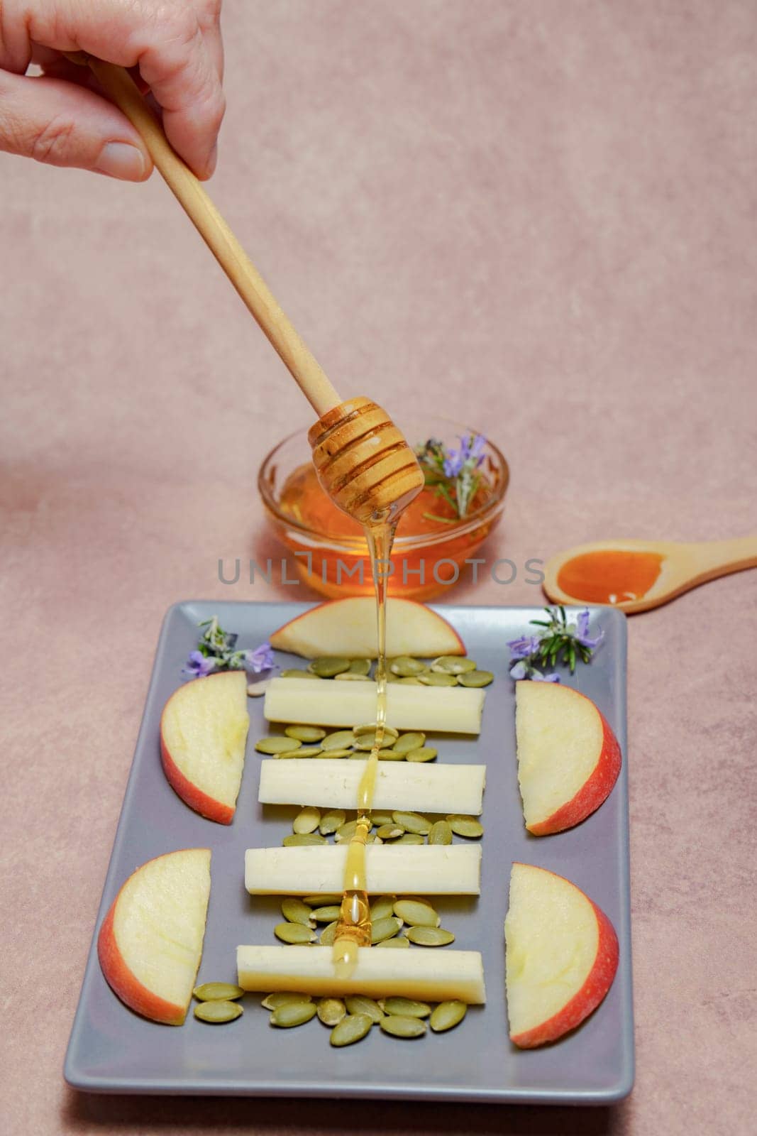 woman sprinkles a wooden spoon with honey on a tray with cheese by joseantona