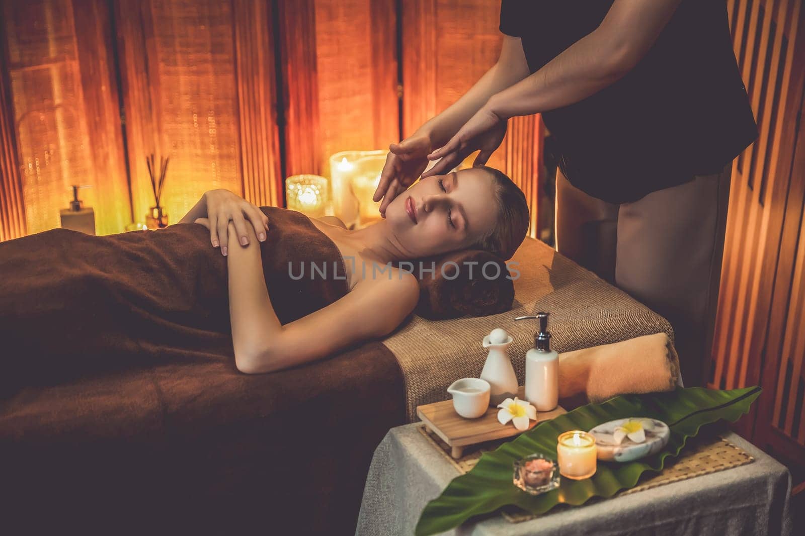 Caucasian woman enjoying relaxing anti-stress head massage and pampering facial beauty skin recreation leisure in warm candle lighting ambient salon spa in luxury resort or hotel. Quiescent