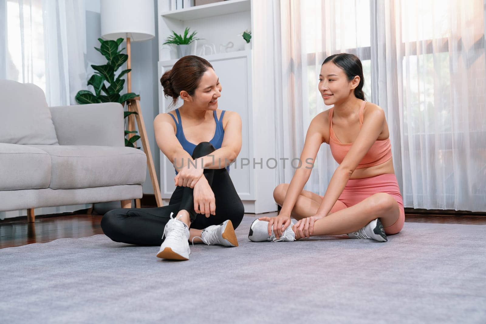 Asian woman in sportswear with her trainer or workout buddy, smiling and posing cheerful gesture. Home workout training or exercise fitness lifestyle in pursuit of healthy lifestyle. Vigorous