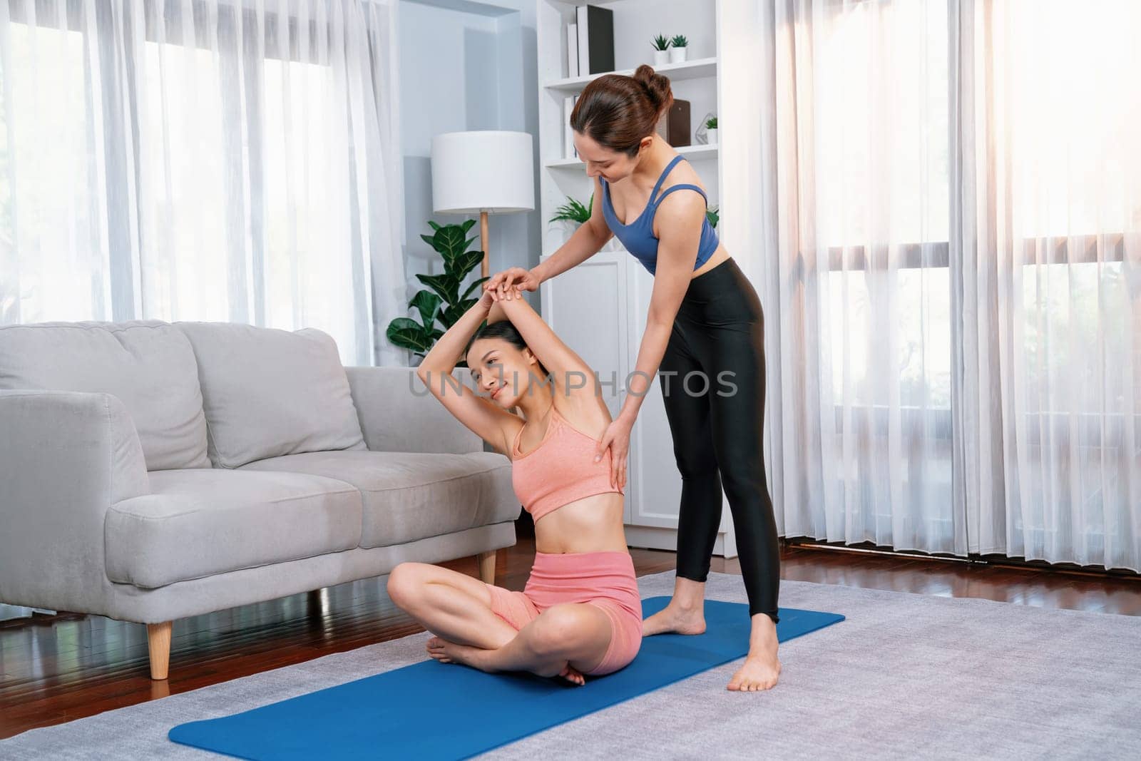 Asian woman in sportswear doing yoga exercise on fitness mat with trainer or workout buddy as home workout training routine. Healthy body care in yoga lifestyle people. Vigorous