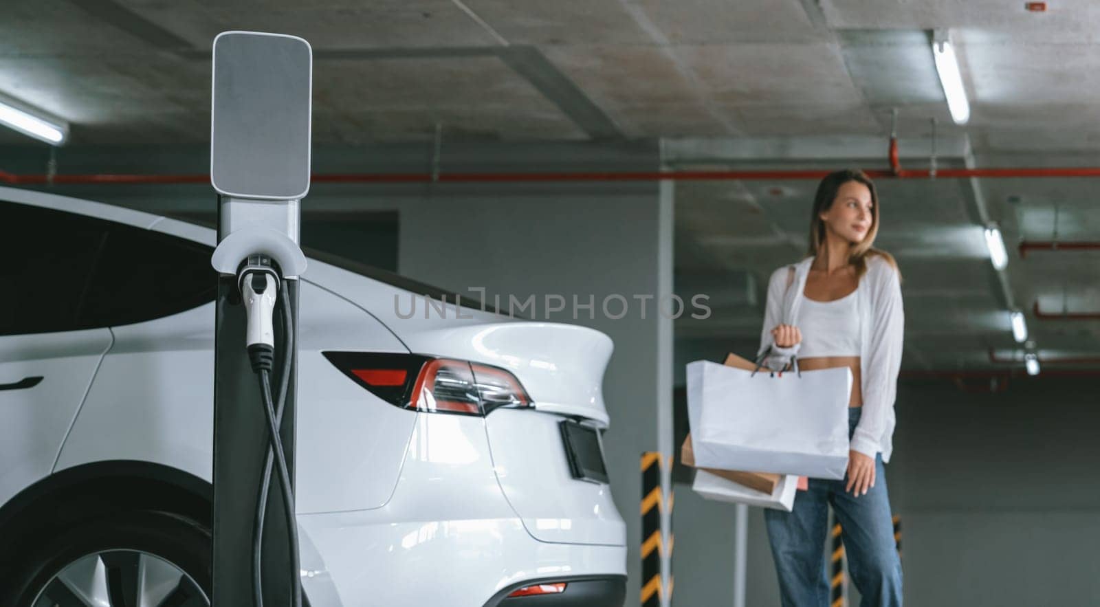 Young woman travel with EV electric car to shopping center parking lot charging in downtown city showing urban sustainability lifestyle by green clean rechargeable energy of electric vehicle innards