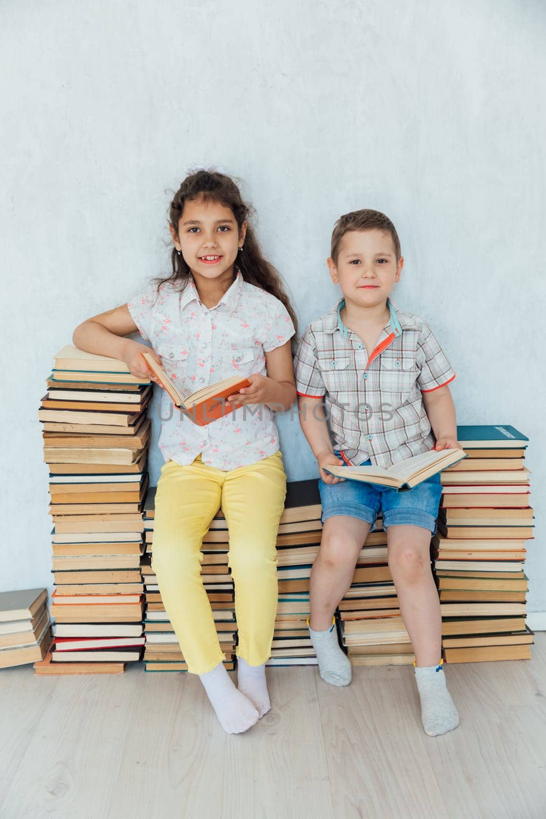 Little boy and girl sitting on stacks of books