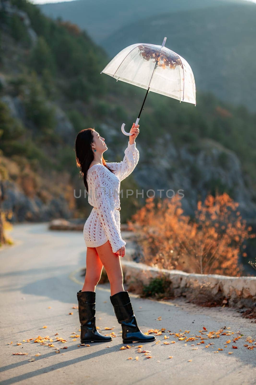 woman umbrella leaves , She holds him over her head, autumn leaves are falling out of him. Beautiful woman in a dress with an umbrella in the autumn park on the road in the mountains. by Matiunina