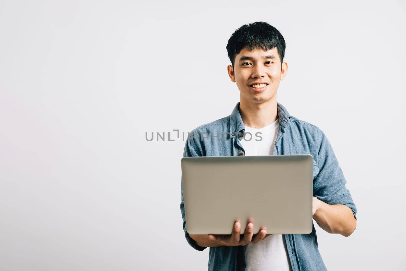 Portrait of a man with a confident smile, typing on a laptop for a successful email or chat session. Studio shot of Asian student isolated on white, showcasing his proficiency in online communication.