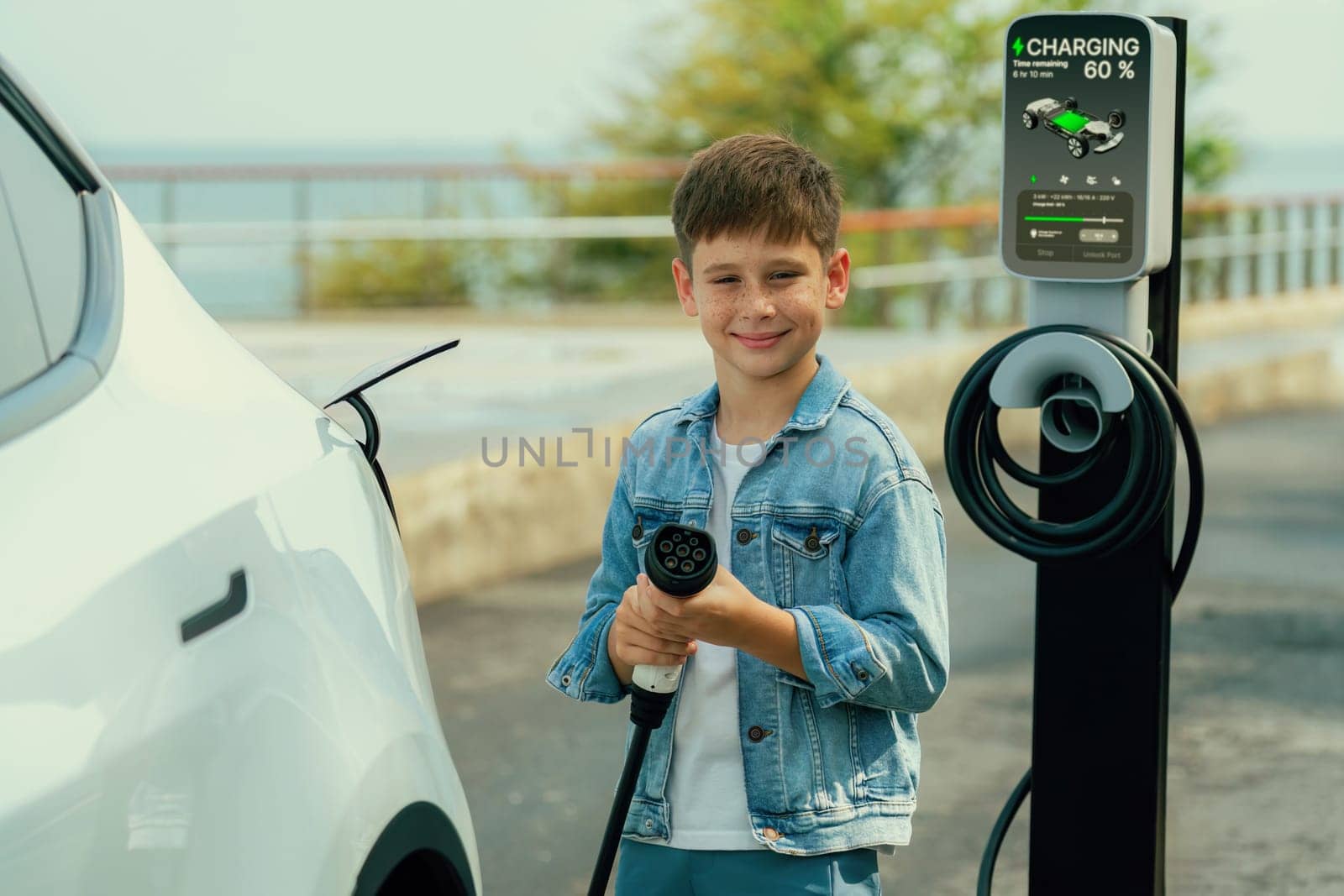 Little boy recharging electric car from EV charging station. Perpetual by biancoblue