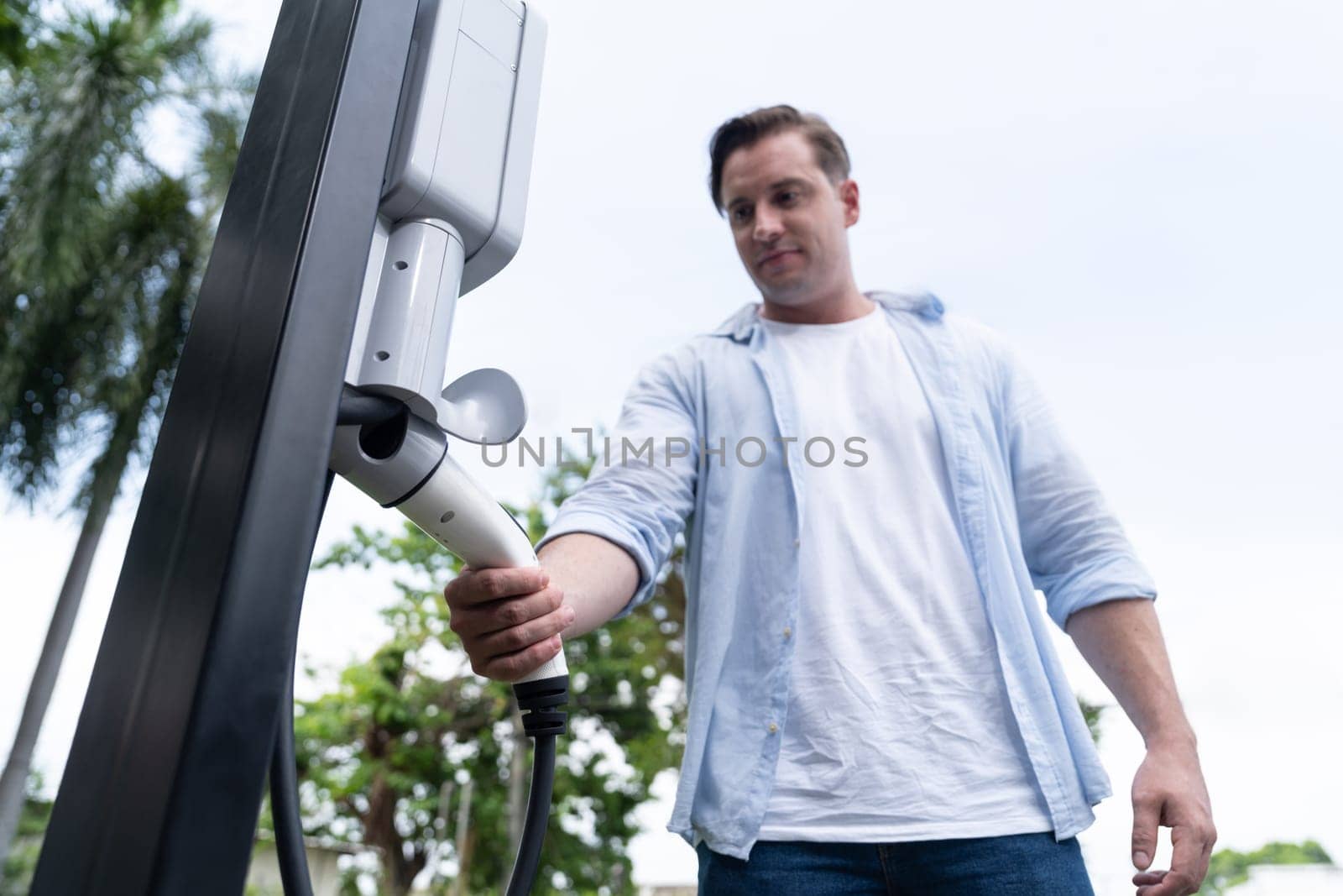 Eco-friendly conscious man recharging modern electric vehicle from EV charging station. EV car technology utilized as alternative transportation for future sustainability. Synchronos