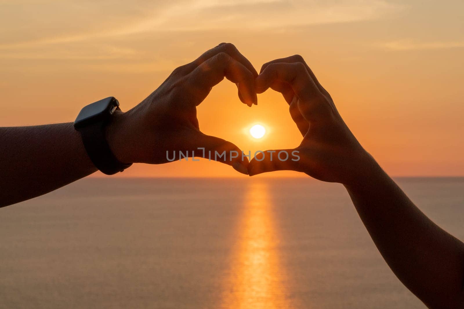 Hands heart sea sanset. The image features a beautiful sunset with two people holding their hands up in the air, forming a heart shape. by Matiunina