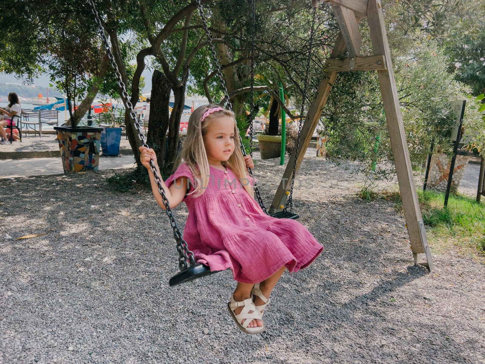 Little girl in a pink dress swings on a chain swing in the park. High quality photo
