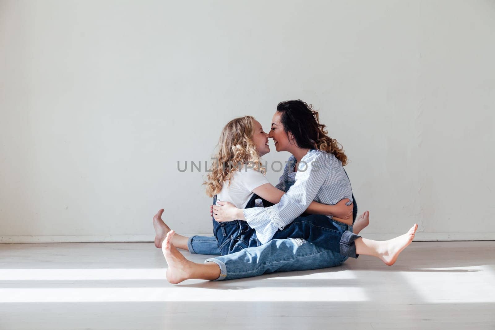 Mom and daughter in jeans sit together cuddling kisses