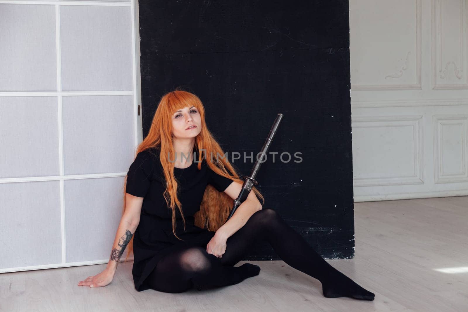 A female cosplayer with red hair sits on the floor holding a Japanese sword