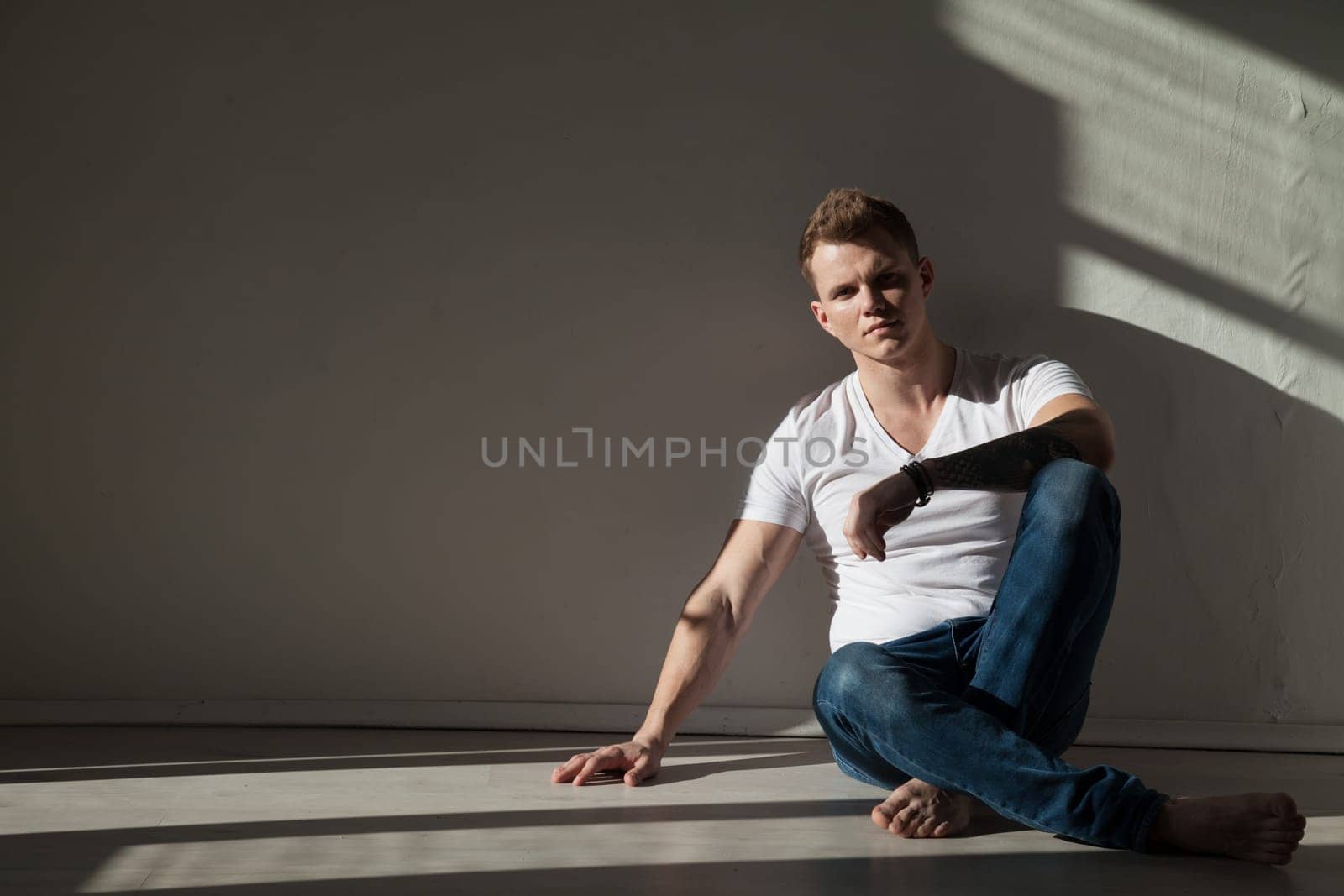 fashionable man in jeans sits on the floor in the room by Simakov
