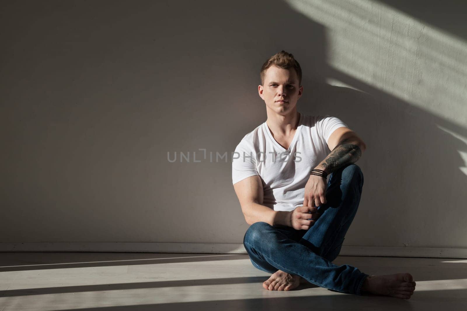 fashionable man in jeans sits on the floor in the room by Simakov