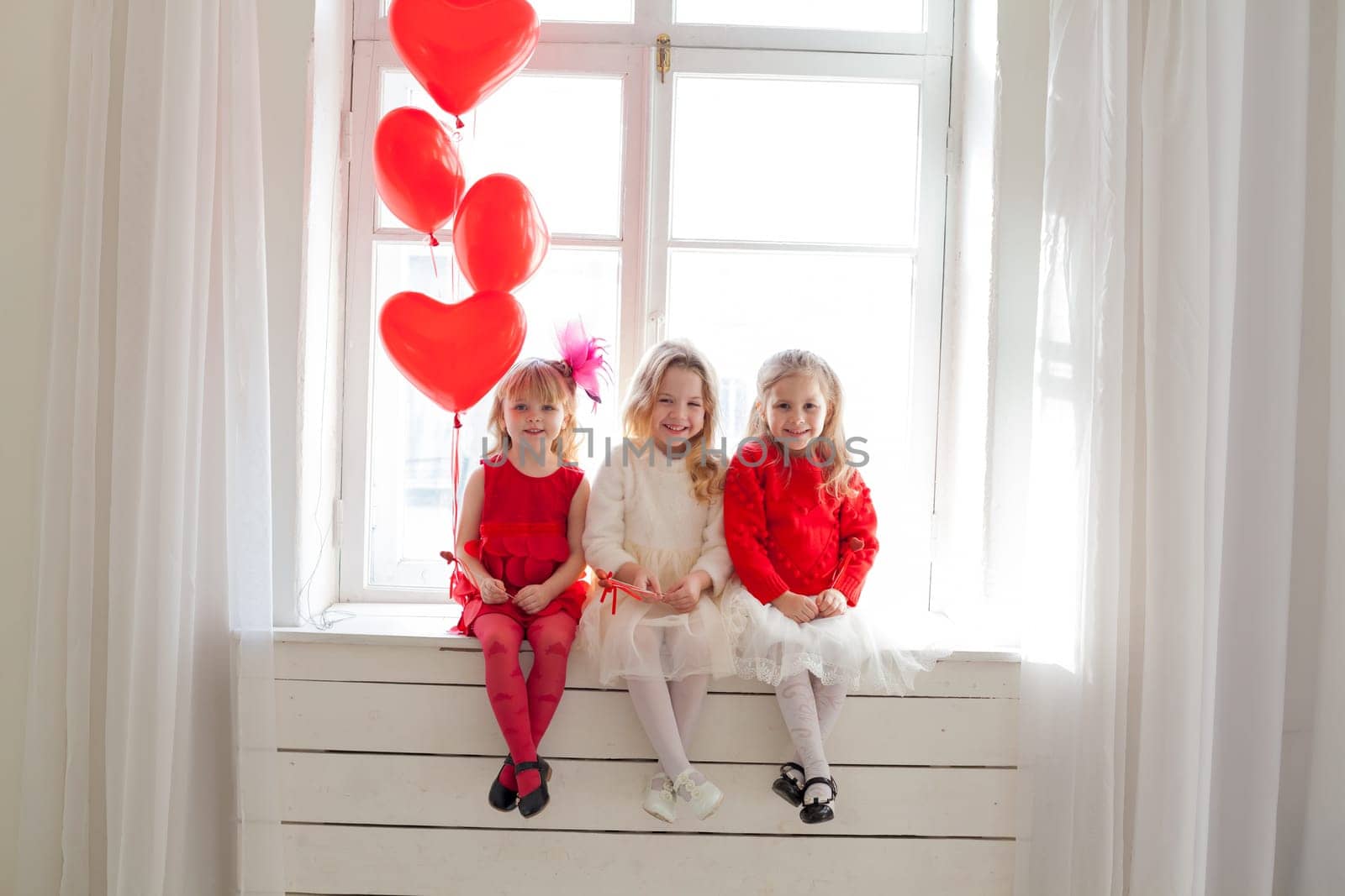 Three girl girlfriends sit by the window with holiday balloons