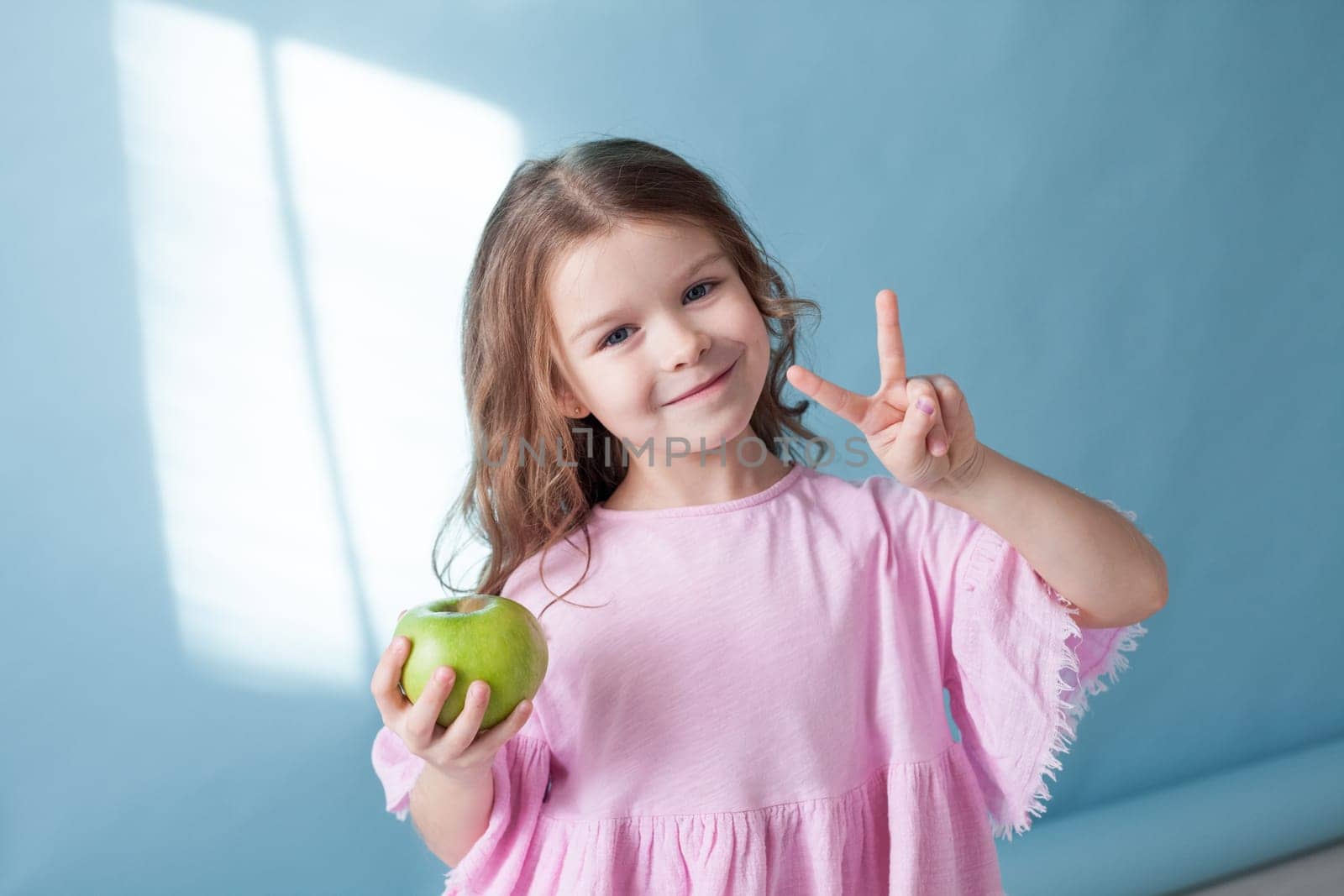 Beautiful little girl with green apple shows two fingers