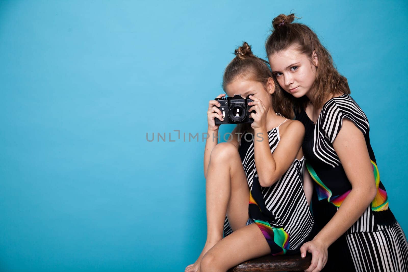 Two fashionable little girls sisters of different ages with a camera by Simakov