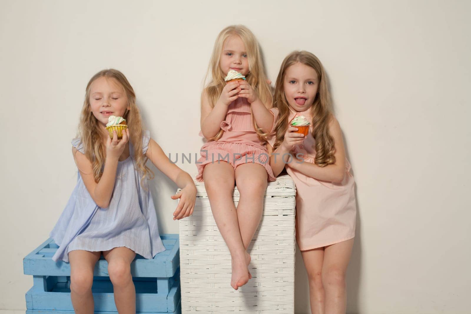 Three fashionable little girls in light dresses eat candy lollipop
