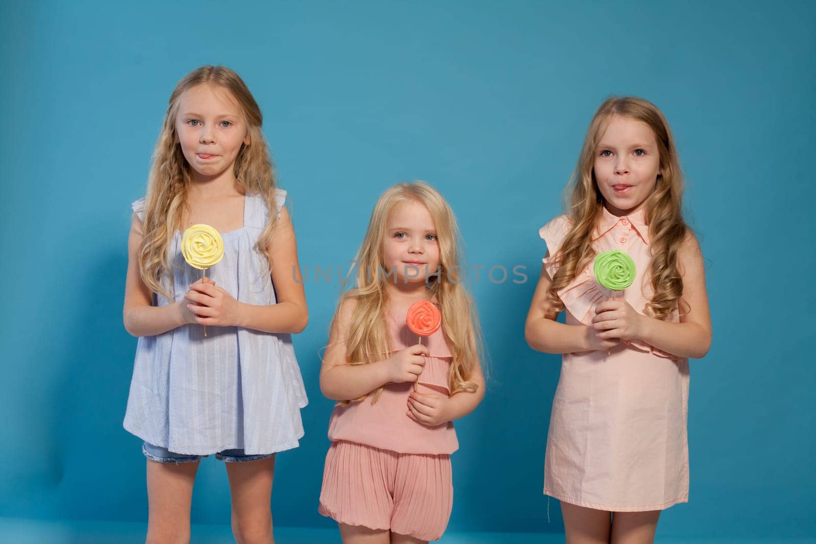 Three fashionable little girls eat candy lollipop by Simakov