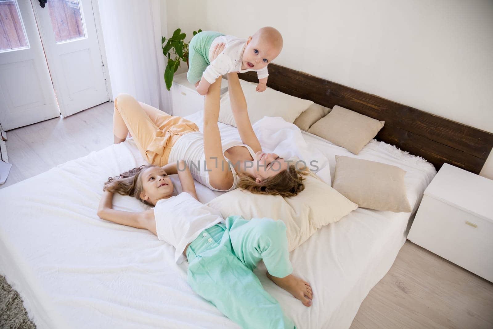 three little girls sisters play in the bedroom on the bed by Simakov