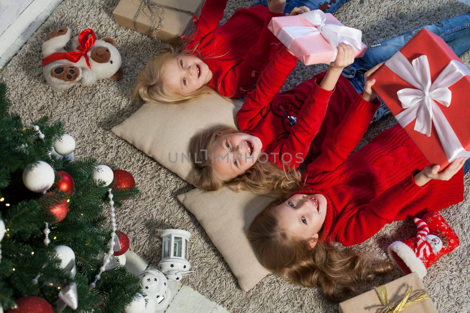 Three girl sisters open Christmas gifts at the Christmas tree new year by Simakov