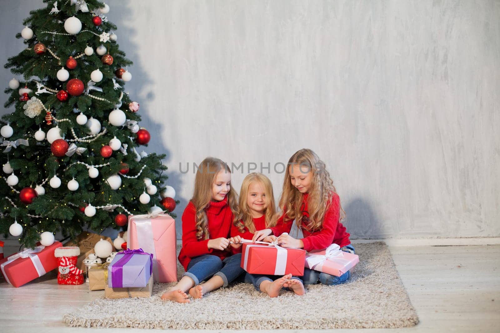 Three little girl girlfriends open Christmas presents to the new year