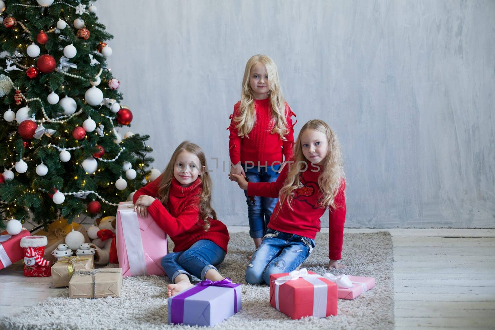 Three girl sisters open Christmas gifts at the Christmas tree new year by Simakov