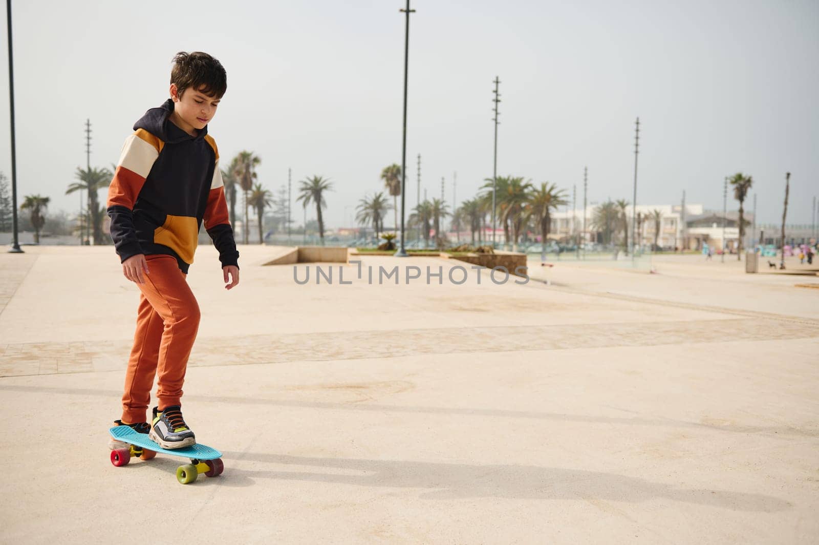 Happy Caucasian elementary age kid boy enjoying skateboarding, riding on skateboard on a skatepark on beautiful sunny day. Childhood. Extreme sport concept. Active healthy lifestyle. Leisure activity