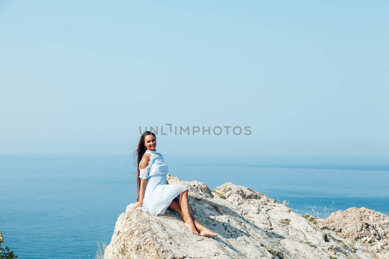a woman with long hair stands on a rock by the blue sea