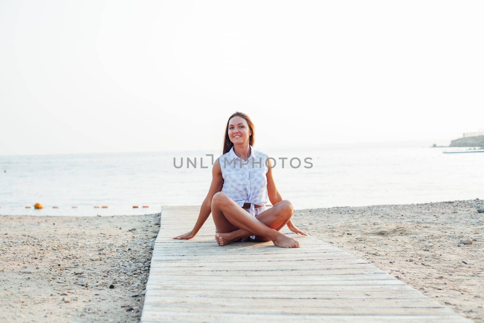 Tanned woman with long hair does yoga on beach by the sea by Simakov