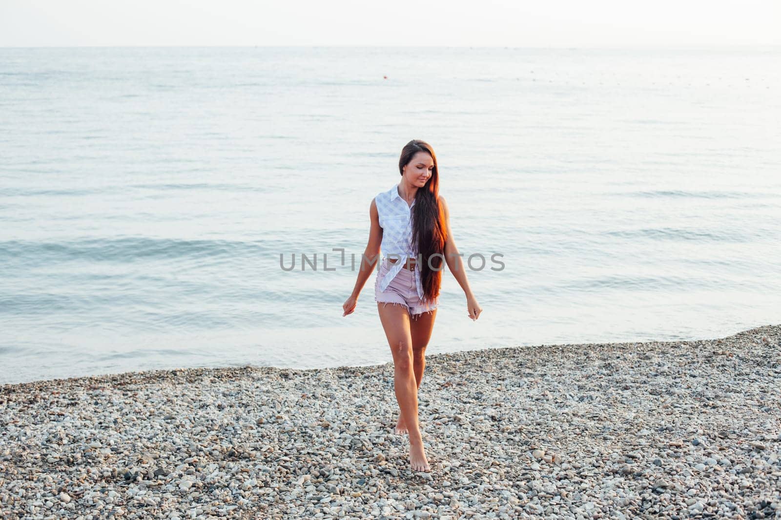 woman with long hair walks on beach by the sea
