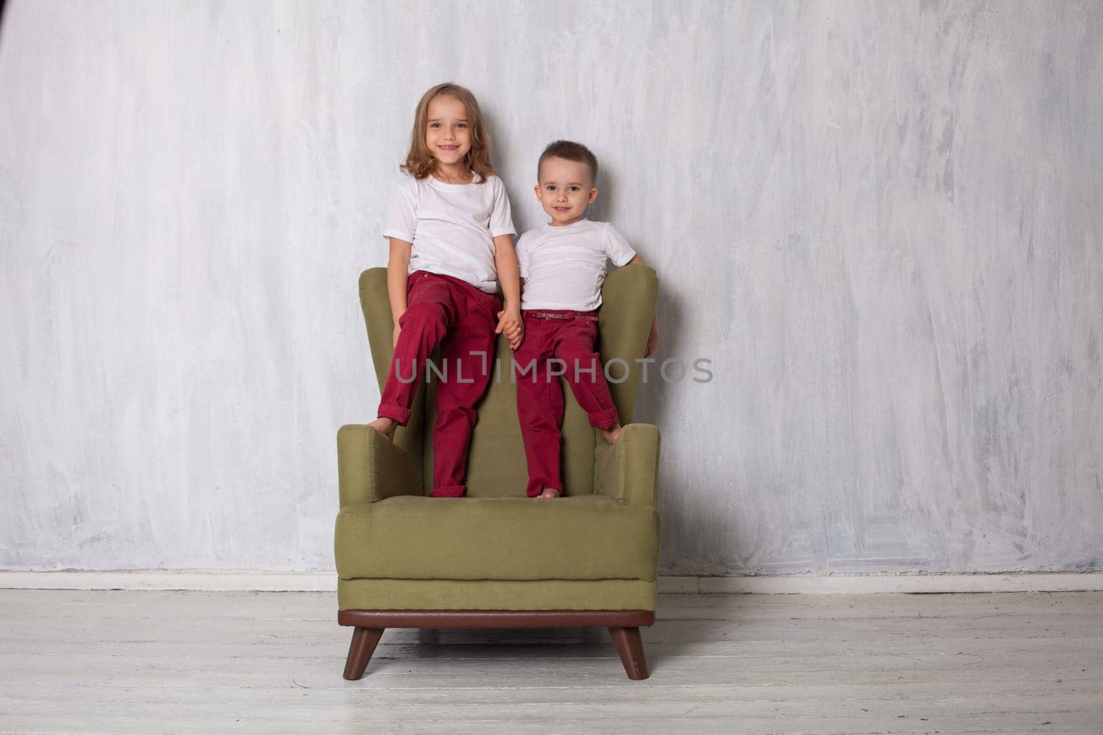 Boy and girl sit in vintage green chair by Simakov