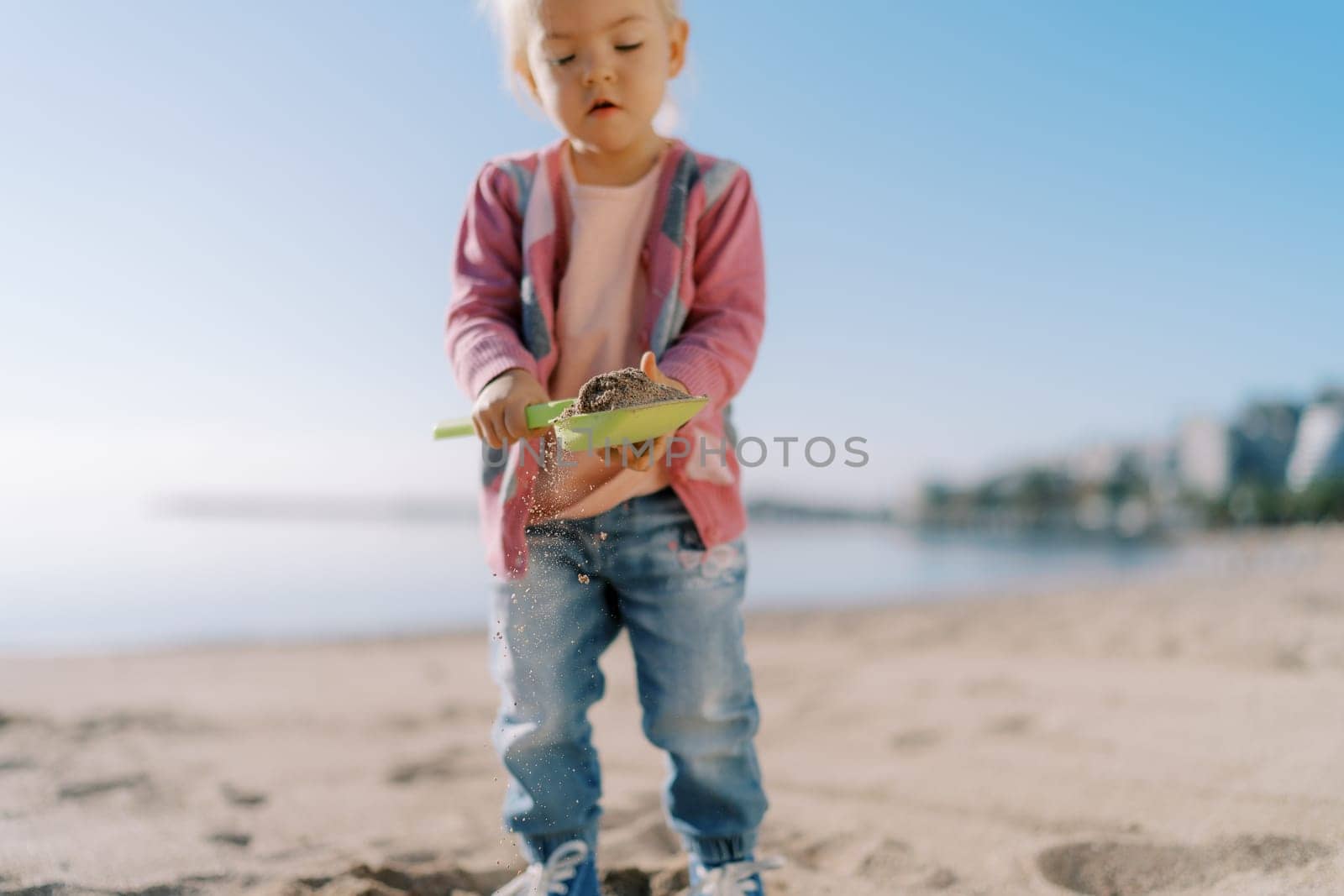 Little girl carries sand on a toy shovel and looks at it. High quality photo