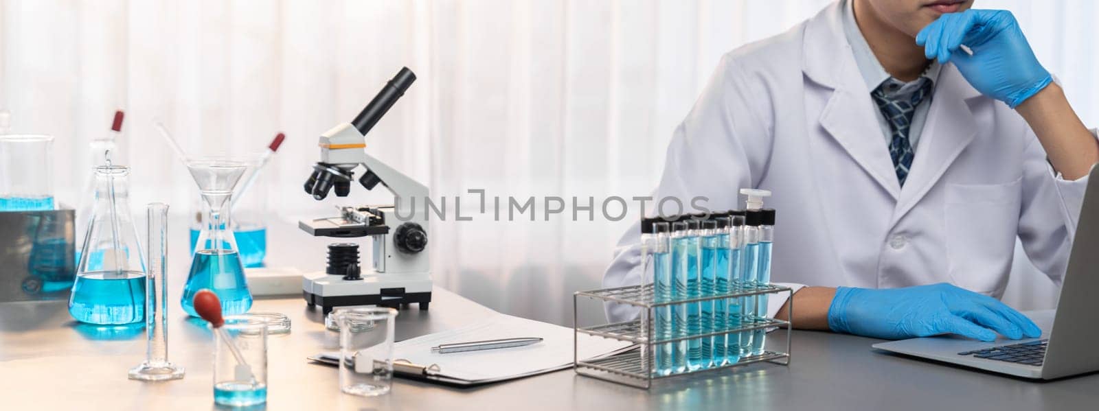 Scientist conduct chemical experiments and research in medical lab as groundbreaking developing for new vaccine drug or antibiotic and studying test result on laptop. Neoteric
