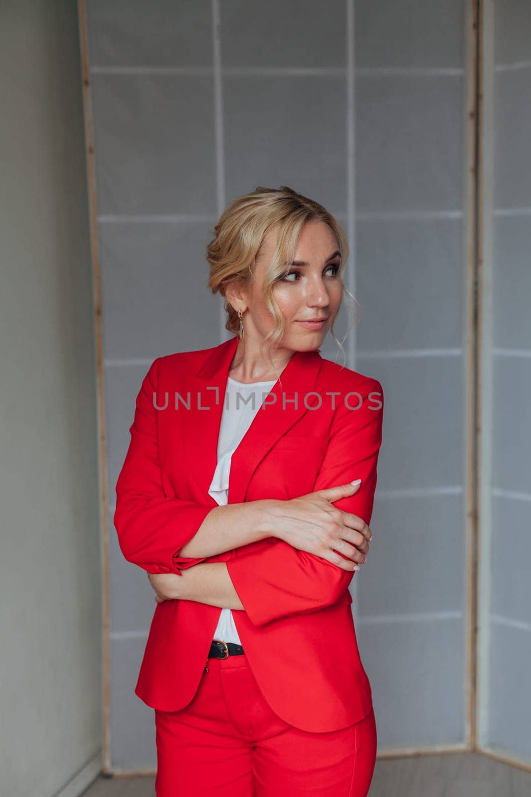 Portrait of a beautiful blonde woman in a red business suit in the office by Simakov