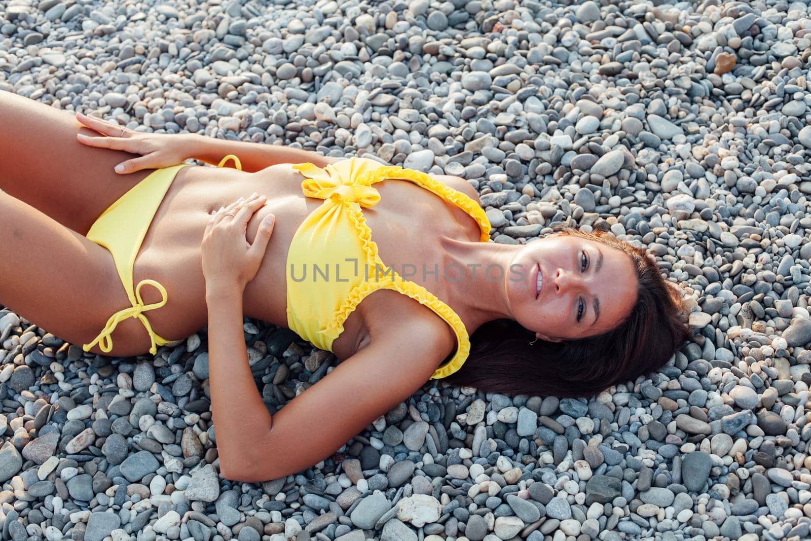 tanned woman in yellow swimsuit sunbathes on the beach