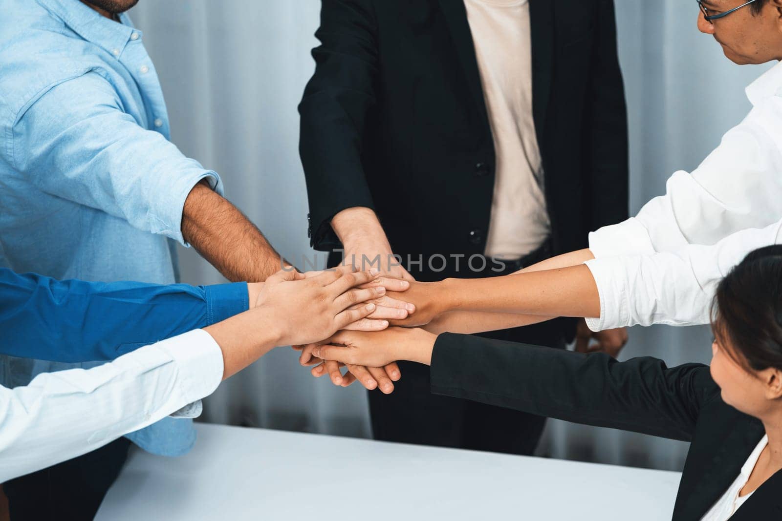 Group of diverse office worker join hand together in office room symbolize business synergy and strong productive teamwork in workplace. Cooperation and unity between business employee. Prudent