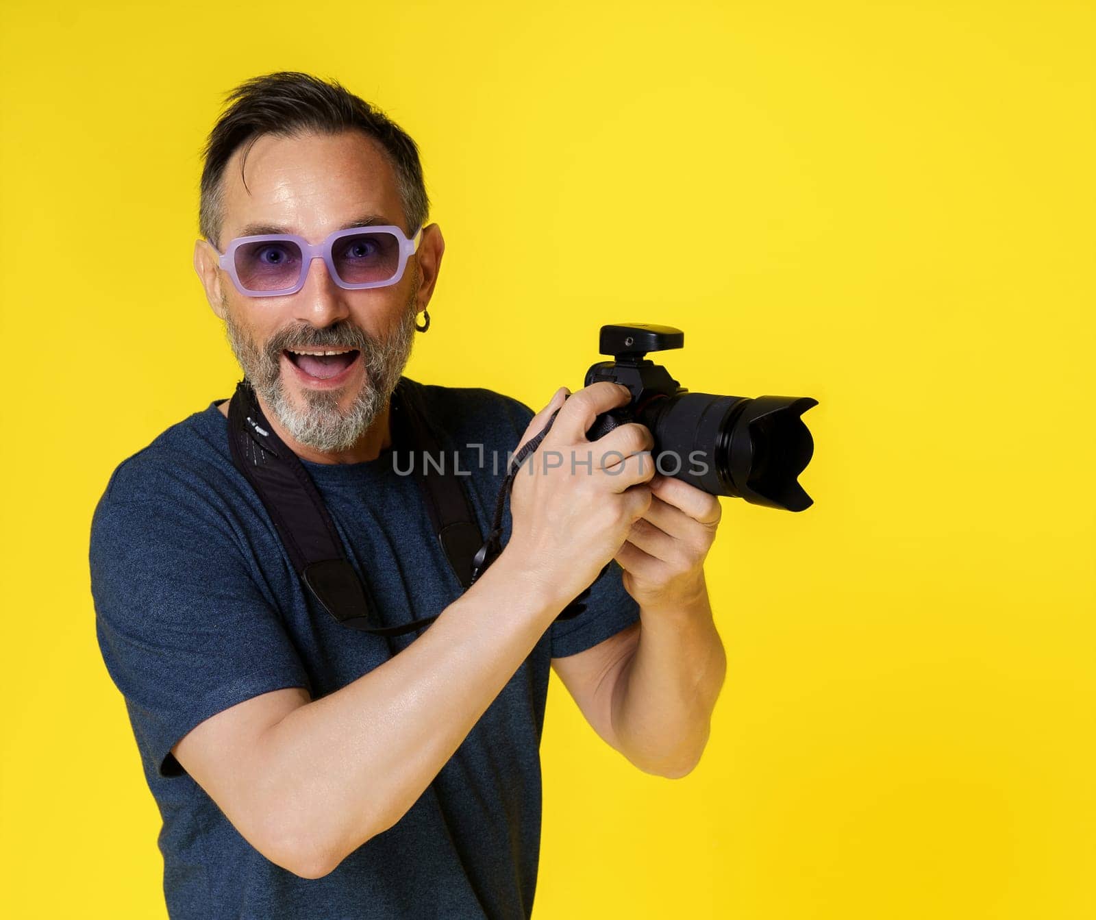 Smiling and happy mid-aged man, passionate about photography, isolated on yellow background, holding digital photo camera. Joy and contentment of mid-aged individual indulging in photography hobby. High quality photo
