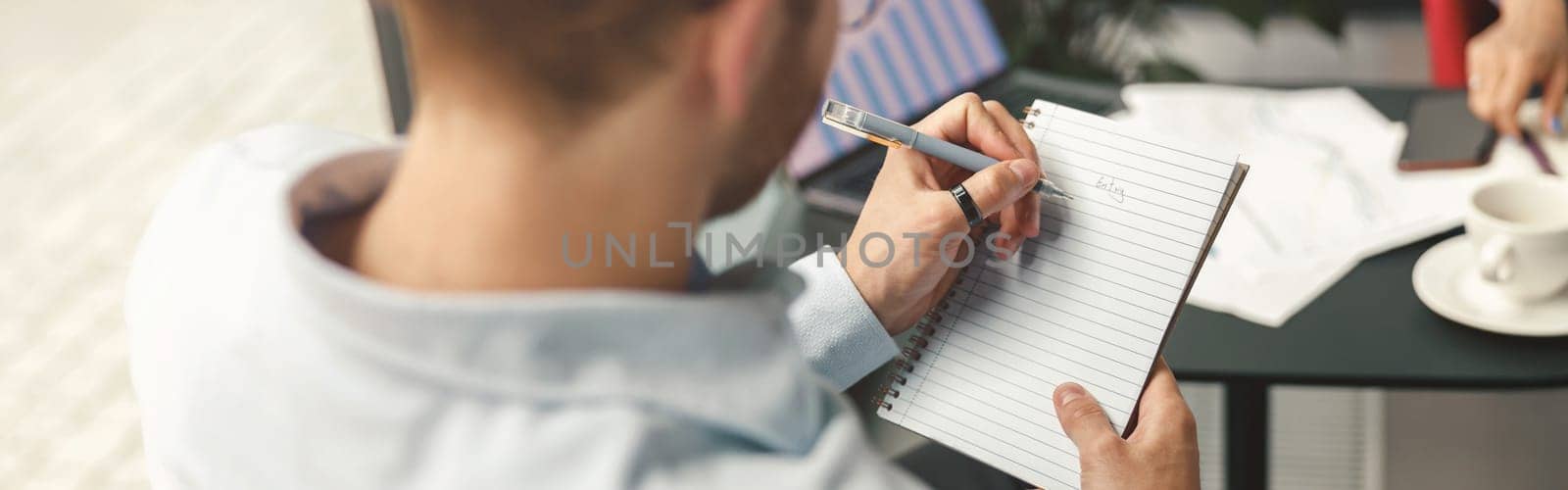Back view of businessman making notes in notepad during meeting in office. High quality photo