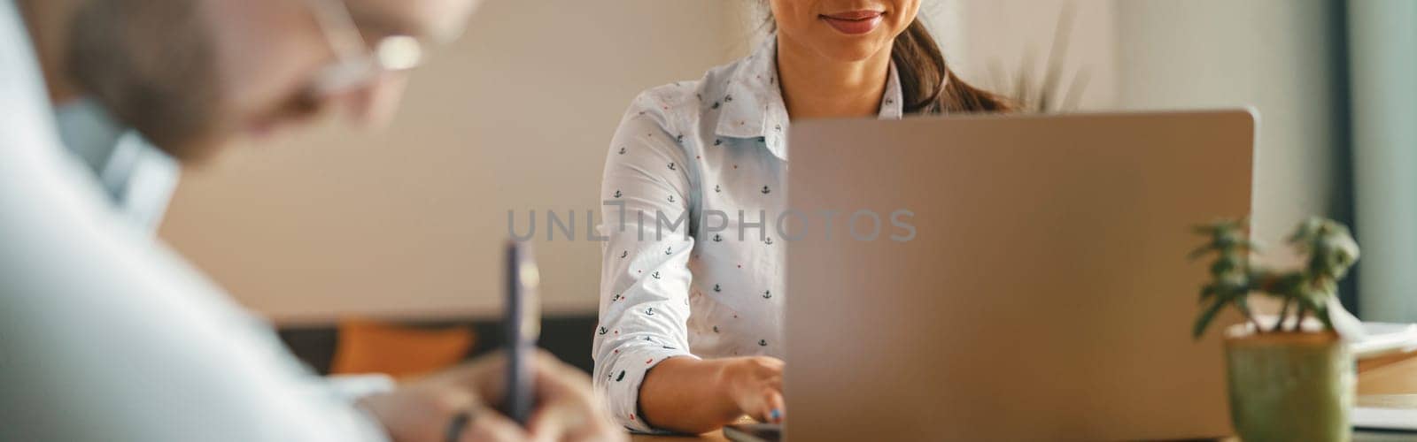 Two coworkers working together on project while using laptop in office meeting room