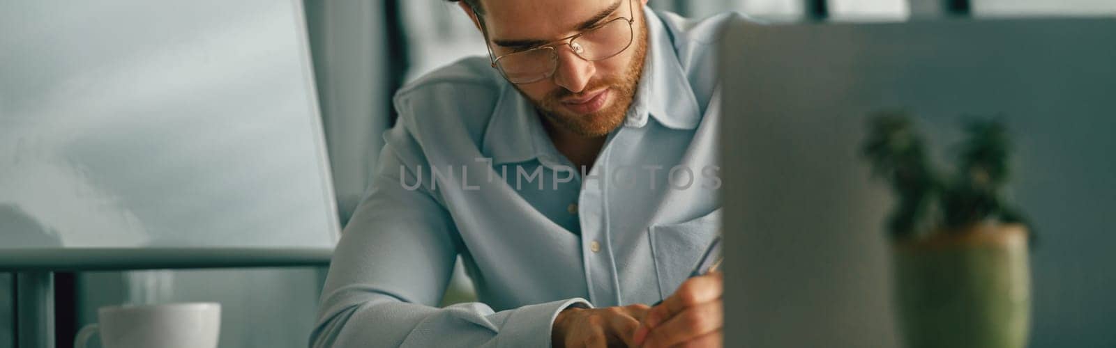 Handsome businessman working on project while using laptop and making notes while sittting in office