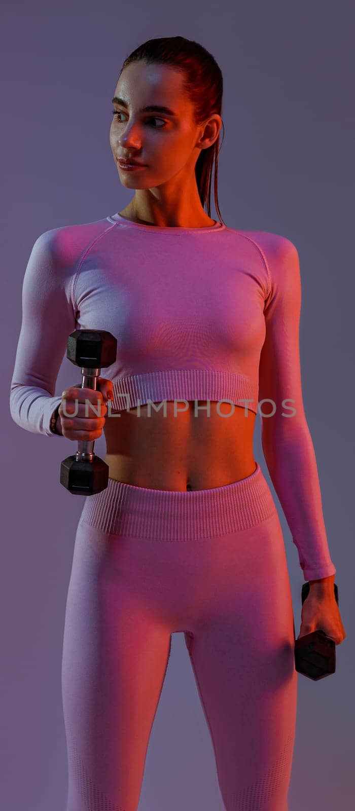 Attractive fitness woman doing exercises with dumbbells on studio background and looking at side by Yaroslav_astakhov