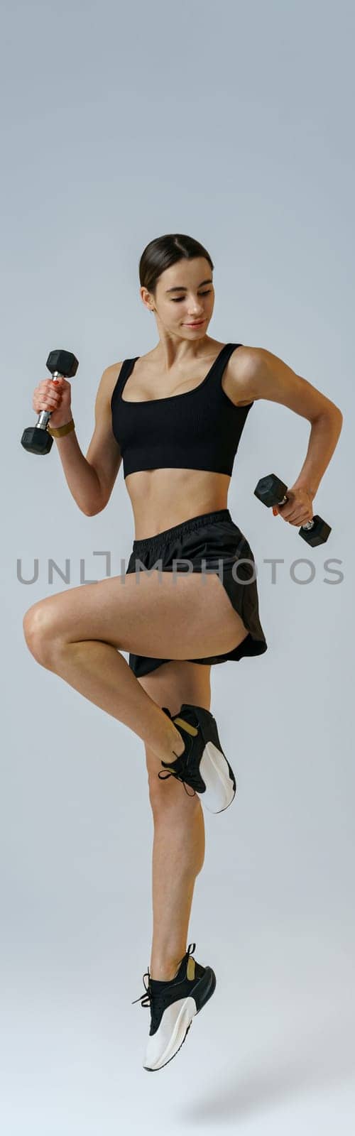 Woman doing cardio exercises with dumbbells on studio background . Healthy lifestyle