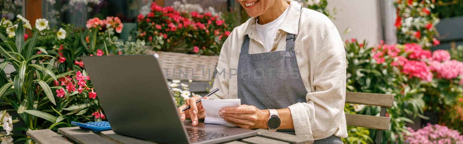 Professional flower shop owner florist using laptop and writing on notebook at flower shop by Yaroslav_astakhov