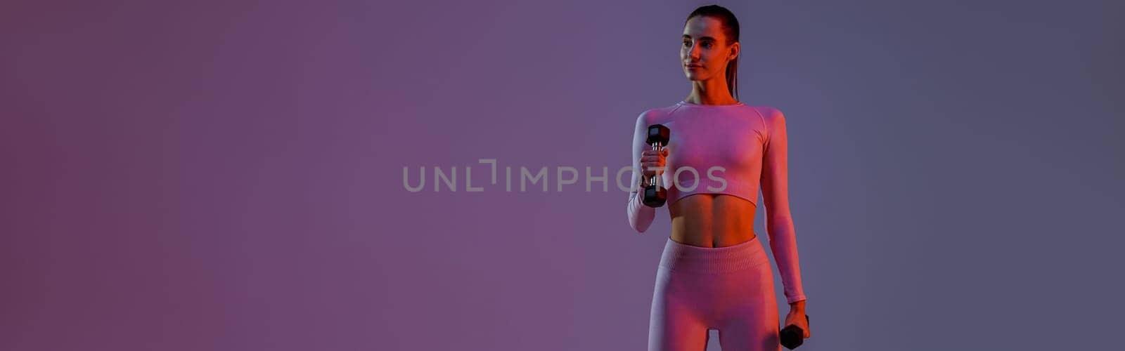 Attractive fitness woman doing exercises with dumbbells on studio background with colored filter by Yaroslav_astakhov