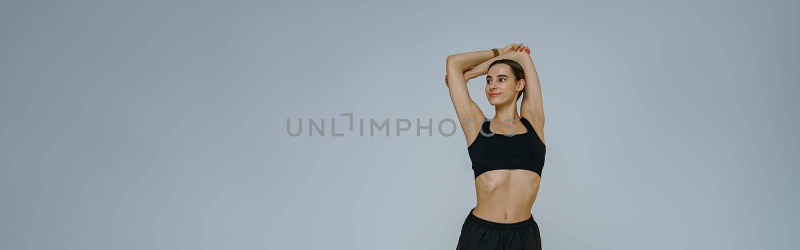 Smiling sporty woman doing warm-up before training session in gym on studio background by Yaroslav_astakhov