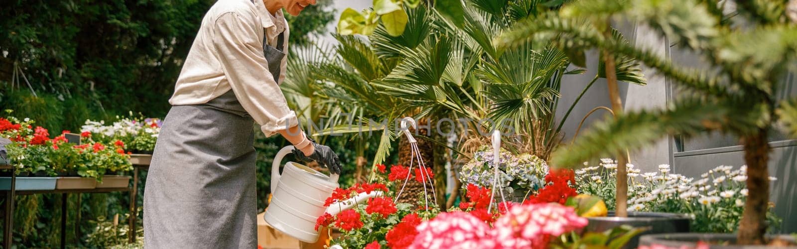 Smiling woman florist taking care of plant watering it in floral shop. High quality photo