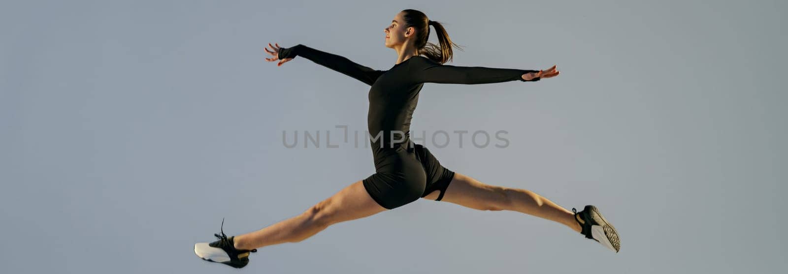 Sporty girl jumping doing split leap in air with joyful expression. Flexible and weightless concept by Yaroslav_astakhov