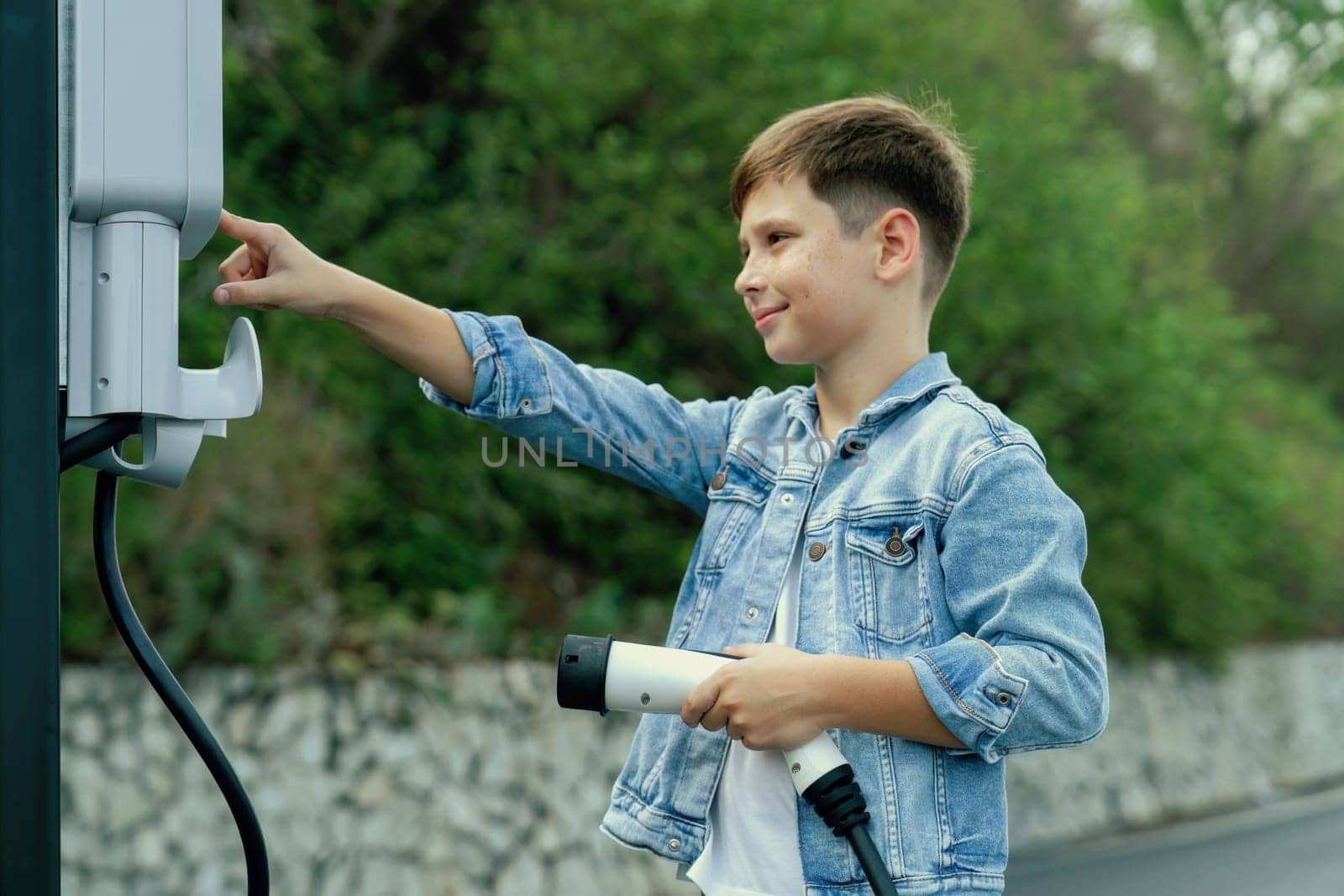 Little boy recharging eco-friendly electric car from EV charging station. EV car road trip travel concept for alternative transportation powered by clean renewable and sustainable energy. Perpetual